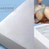 Witte katoenen topper of matrasbeschermer met stiksels en katoenbollen.