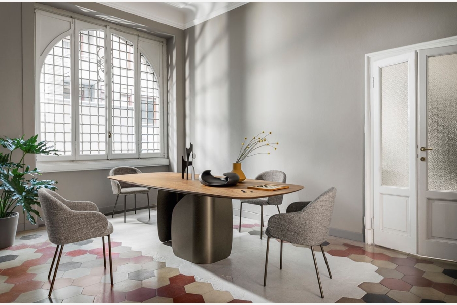 Moderne eettafel met houten blad en grijs onderstel, omringd door gestoffeerde stoelen, in een kamer met mozaïekvloer.