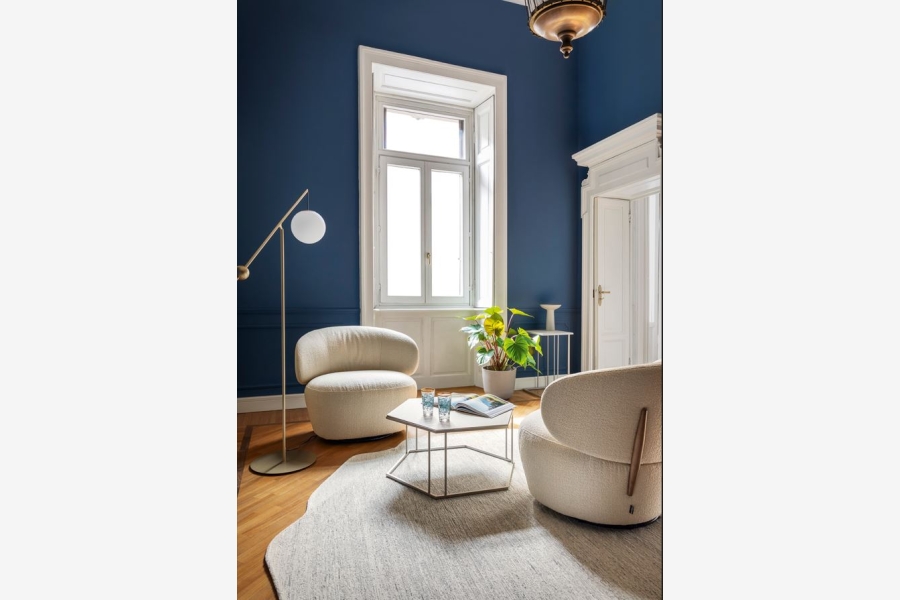 Zitruimte met donkerblauwe muren, een crèmekleurige fauteuil, een staande lamp en een bijzettafel met plant.