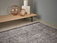 Grijs, hoogpolig vloerkleed in een modern interieur met een lage houten bijzettafel.