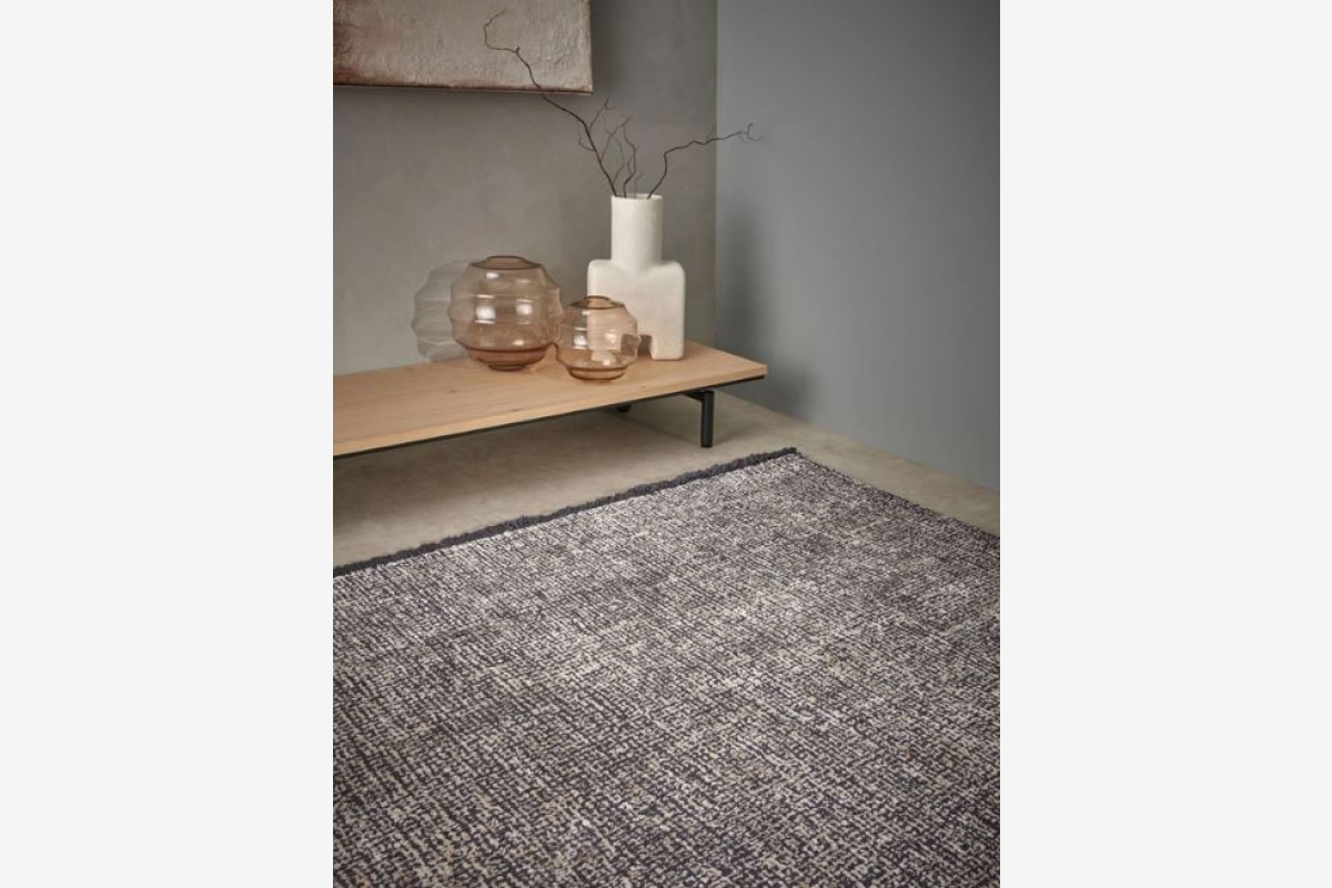 Grijs, hoogpolig vloerkleed in een modern interieur met een lage houten bijzettafel.
