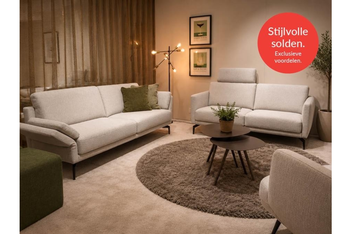 Woonkamer met grote beige bank, kleinere beige bank, ronde salontafel en groene