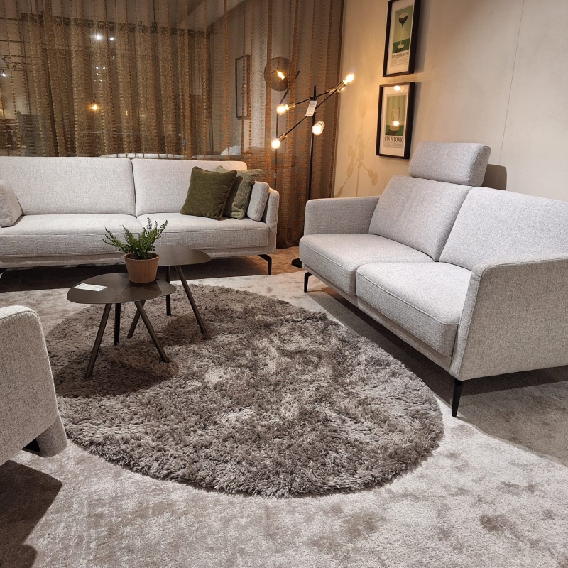Een lichte zithoek met twee grijze banken en een bijpassende fauteuil, met een g