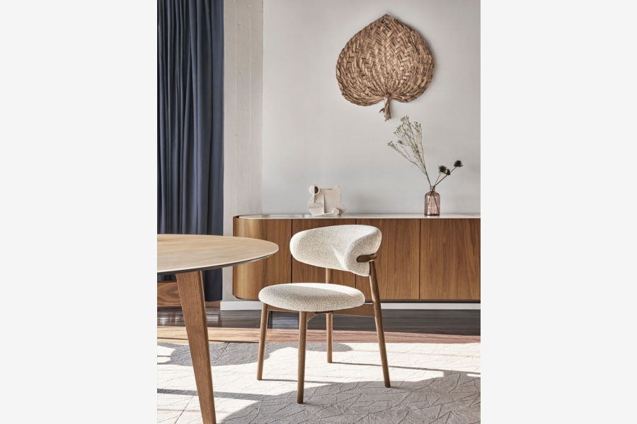 Ronde houten eettafel en een witte stoel in een lichte woonkamer.