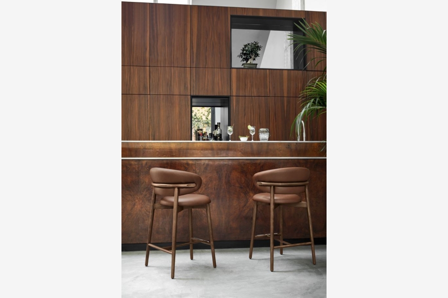 Twee bruine barstoelen met metalen onderstel bij een houten bar met wandpanelen.