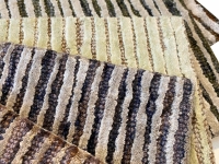 Gestreept dekentje in zwart en beige op een beige, geribbeld oppervlak.
