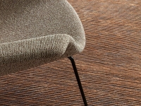 Detail van een lichtbruine stoel met zwarte poten op een bruin gestreept vloerkleed.