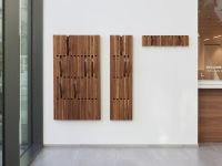 Drie decoratieve houten panelen aan een witte muur naast een raam.