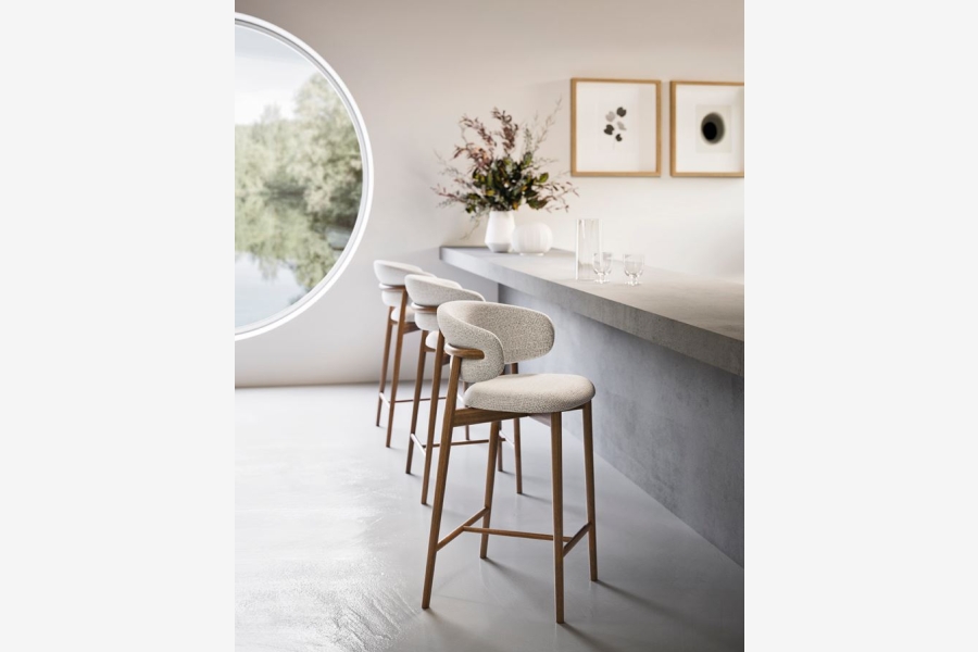 Drie barkrukken met lichte stoffen bekleding en houten poten staan aan een betonnen bar in een moderne ruimte.