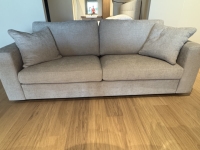 Lichtgrijze tweezitsbank met twee bijpassende kussens op een houten vloer.