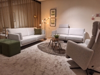 Woonkamer met twee lichtgrijze banken, een fauteuil en twee groene poefs rond ee