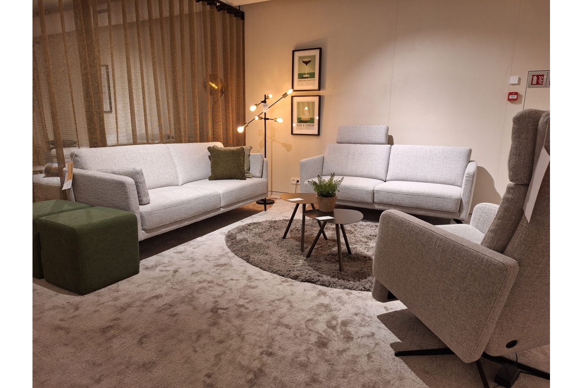 Woonkamer met twee lichtgrijze banken, een fauteuil en twee groene poefs rond ee