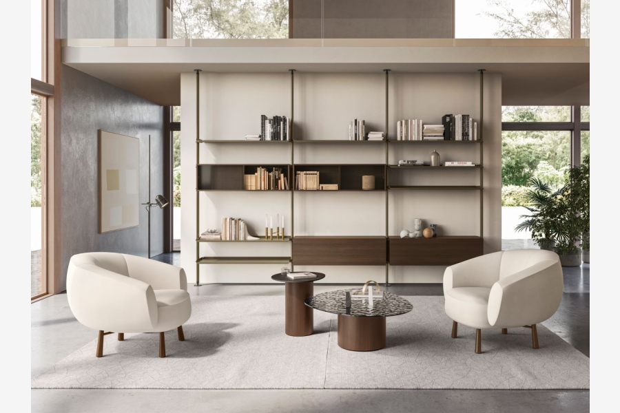 Witte fauteuils met een ronde salontafel voor een kast met open vakken in een lichte woonkamer.
