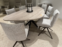 Ovale eettafel met houtnerf en zes stoffen eetkamerstoelen met draaivoet in een